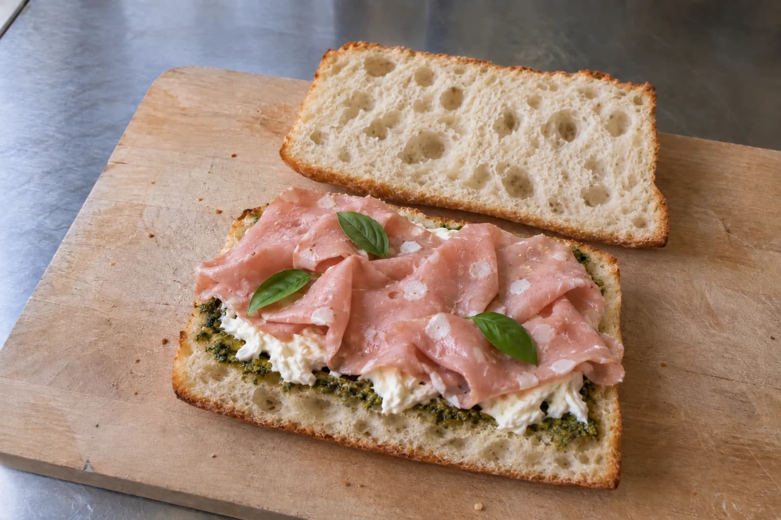 Soft focaccia with pesto, stracciatella, loosely folded mortadella, and basil