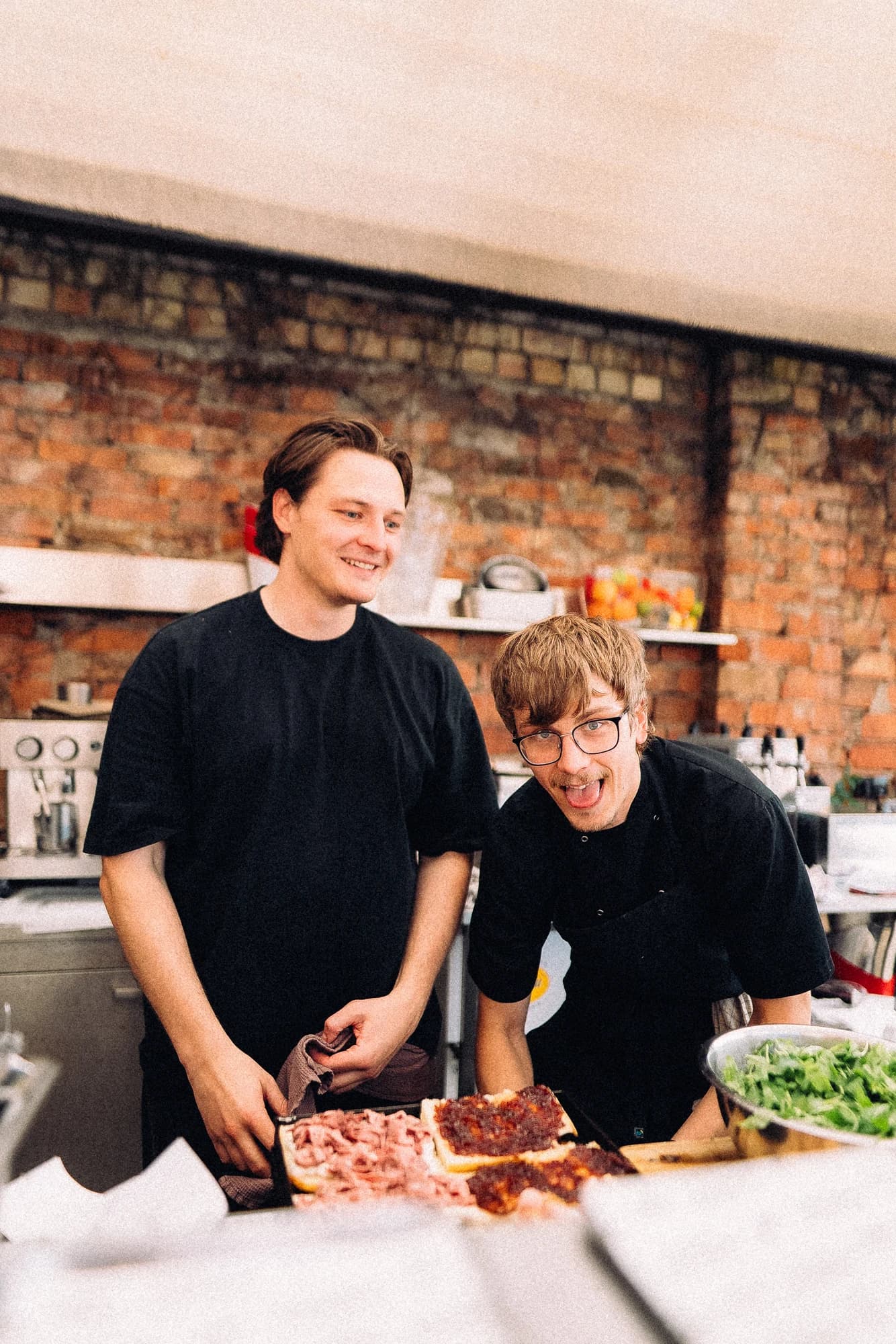 Two sandwich shop teammates behind open focaccia sandwiches at the kitchen counter.